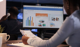 Office employee analyzing business charts on computer and documents, looking at online research data to create presentation. Working with information on report, statistics on pc.